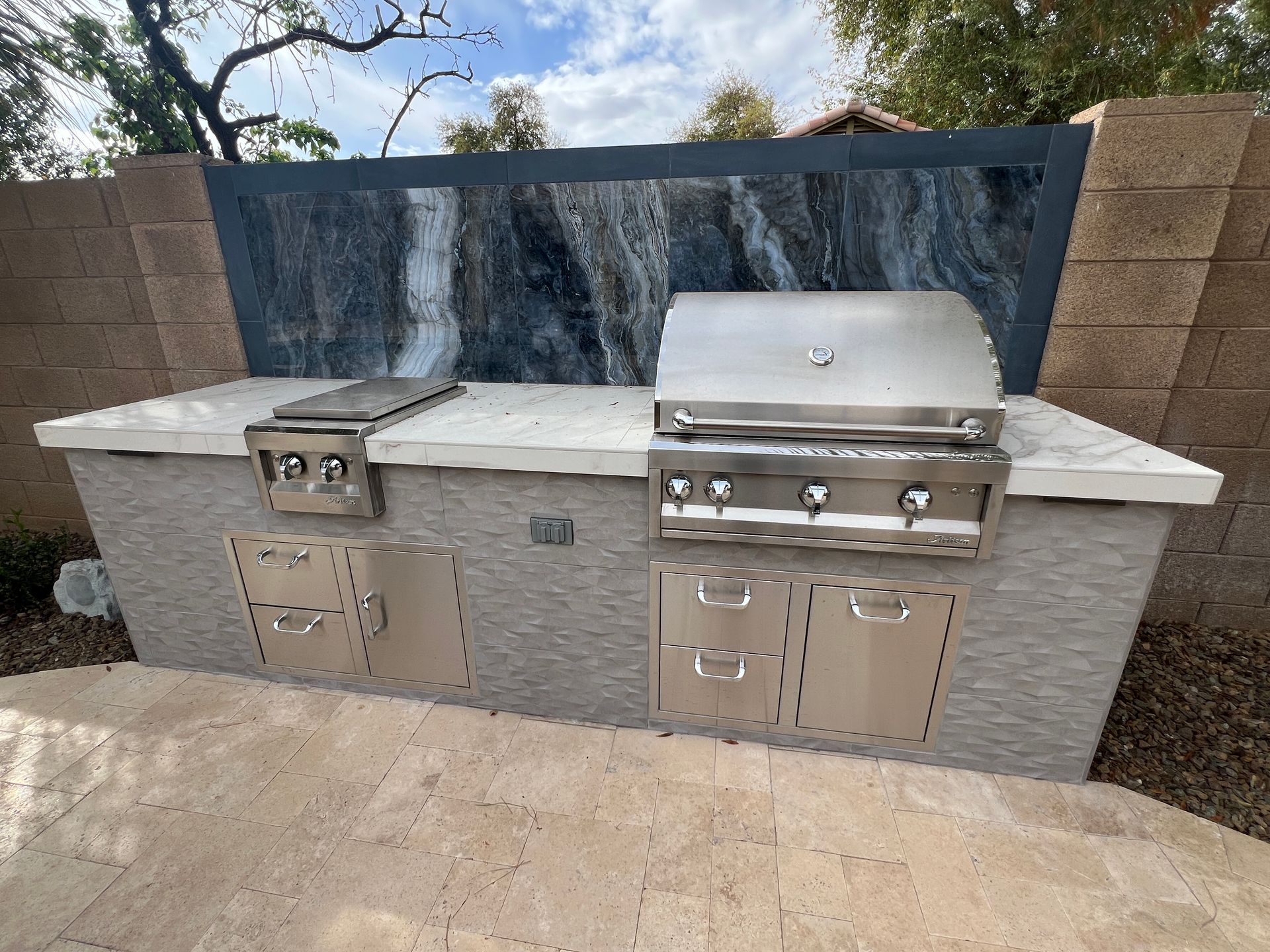 Outdoor kitchen with stainless steel grill, countertop, and stone facade.