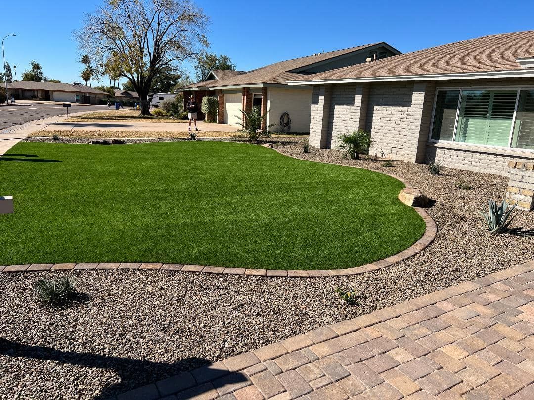 Well-maintained lawn in front of a house, bordered by brown gravel and brick walkway.