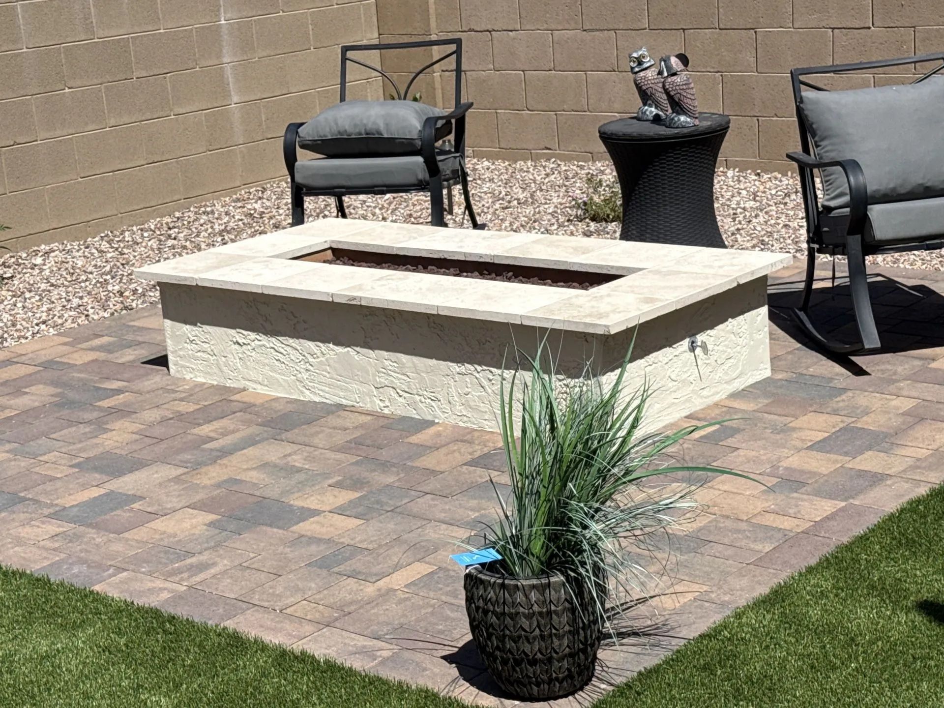 Fire pit on a patio with two chairs and a decorative side table.