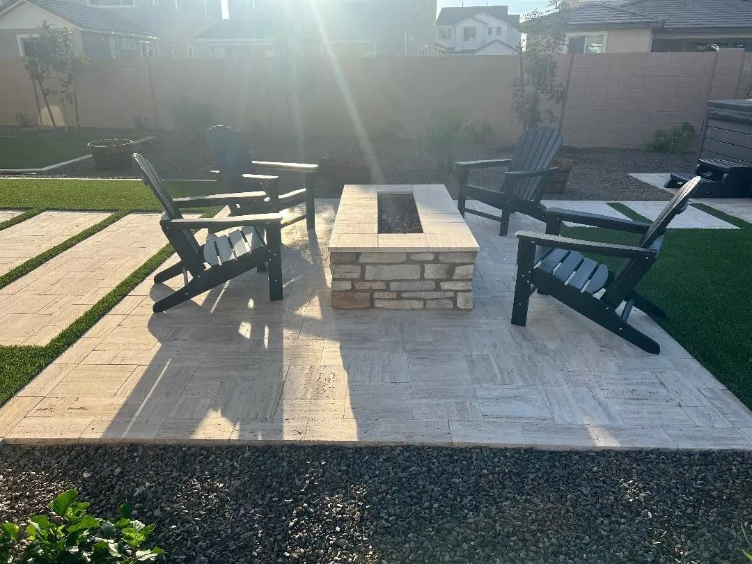 Outdoor seating area with fire pit, chairs, and stone patio. Green grass borders.