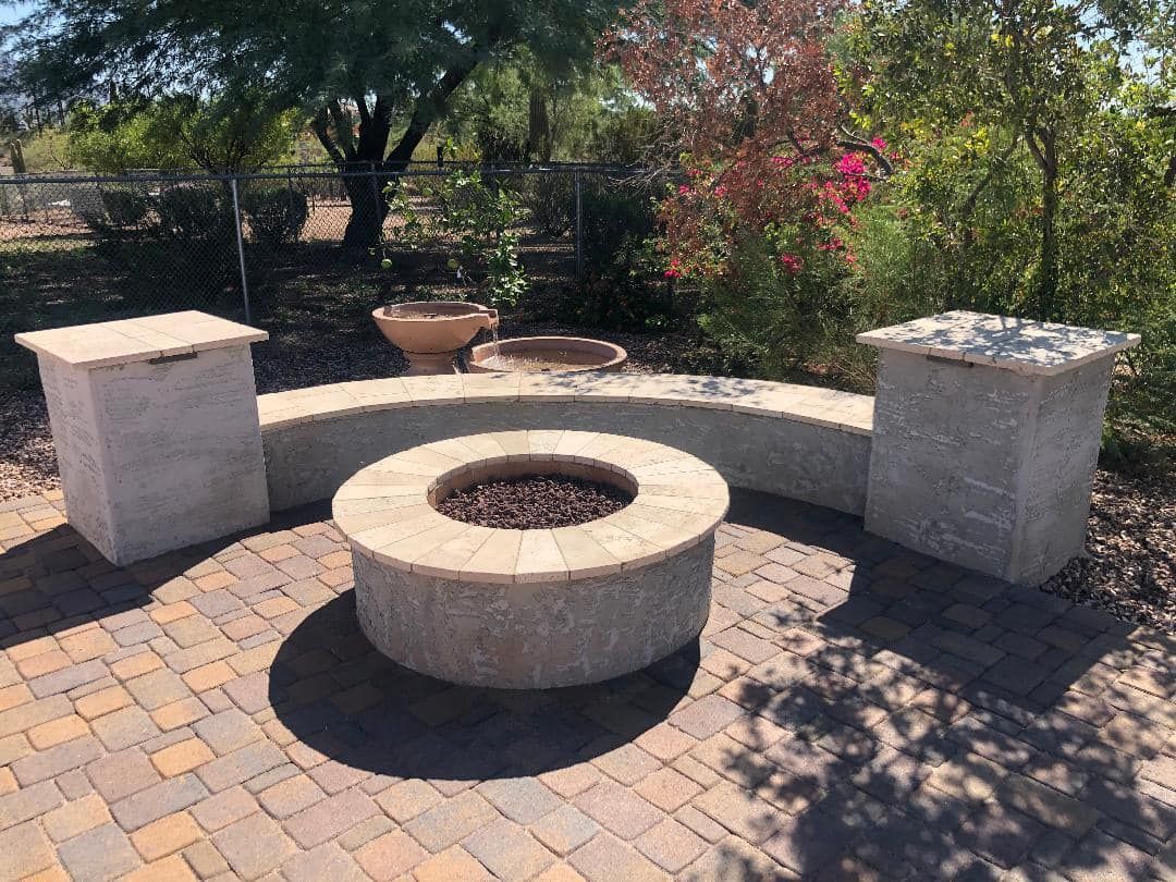 Fire pit and curved bench in patio with brick pavers and two square pillars.