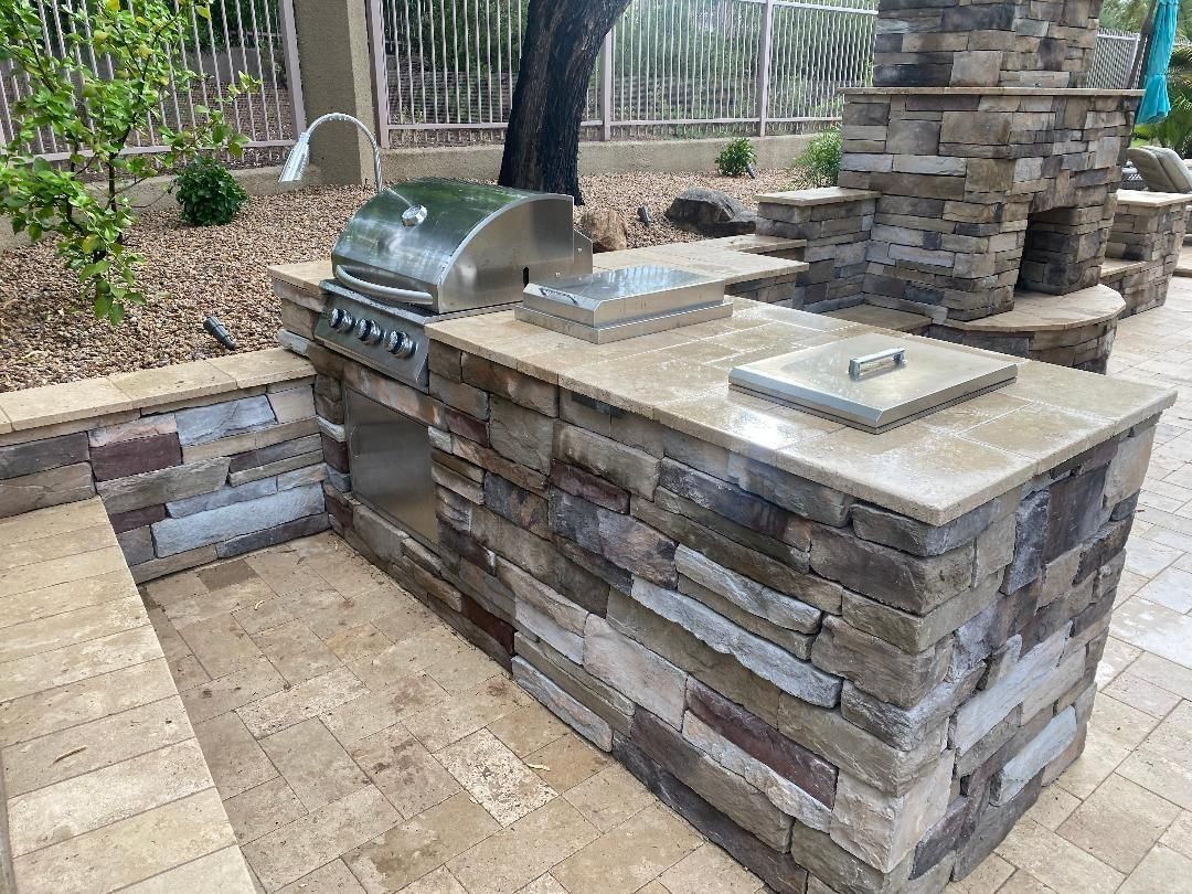 Outdoor kitchen with stone counters, grill, and built-in features on a patio.
