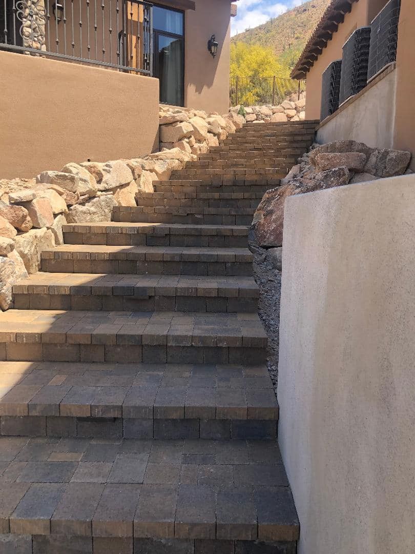 Stone steps leading upward between tan stucco walls and a rocky retaining wall.