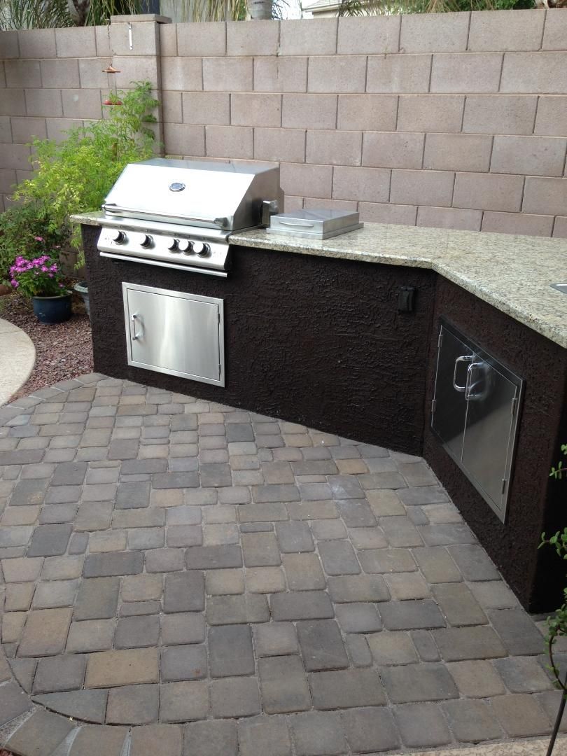 Outdoor kitchen with granite countertop, stainless steel grill, and brick facade on a paver patio.