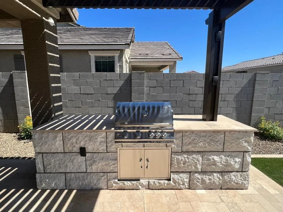 Outdoor kitchen with a built-in grill, stone walls, and a pergola overhead.