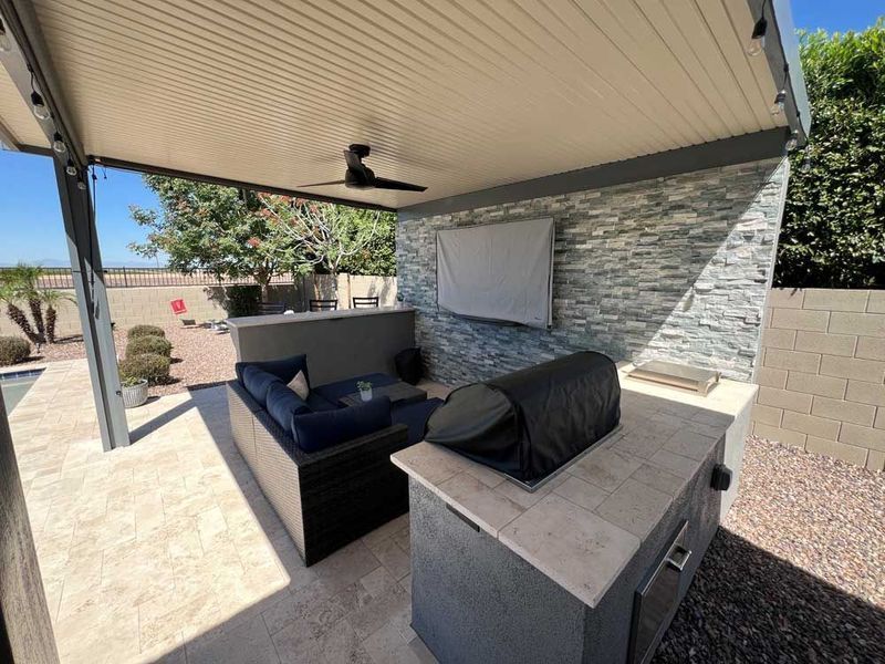 Outdoor kitchen and lounge area with a covered patio, grill, TV, and seating.