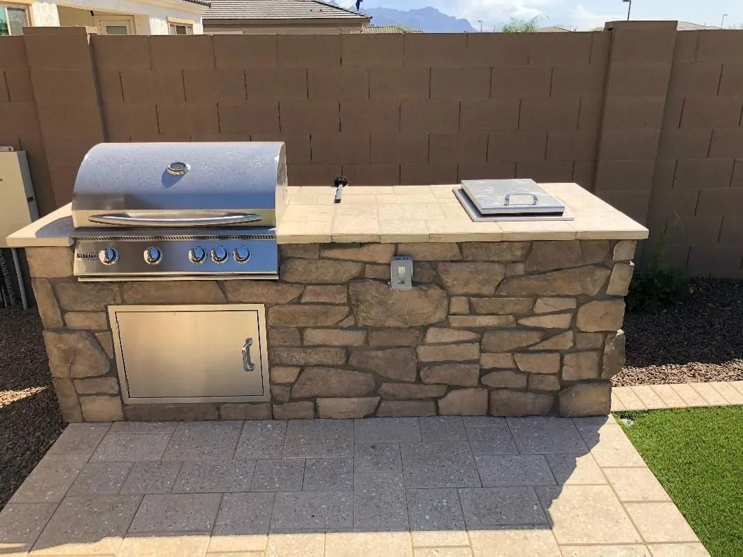 Outdoor stone BBQ island with stainless steel grill, side burner, and storage door.