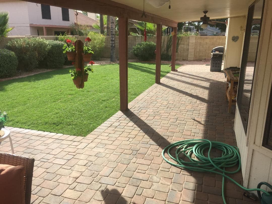 Patio with brick pavers, green lawn, hose, and a covered wooden beam structure.