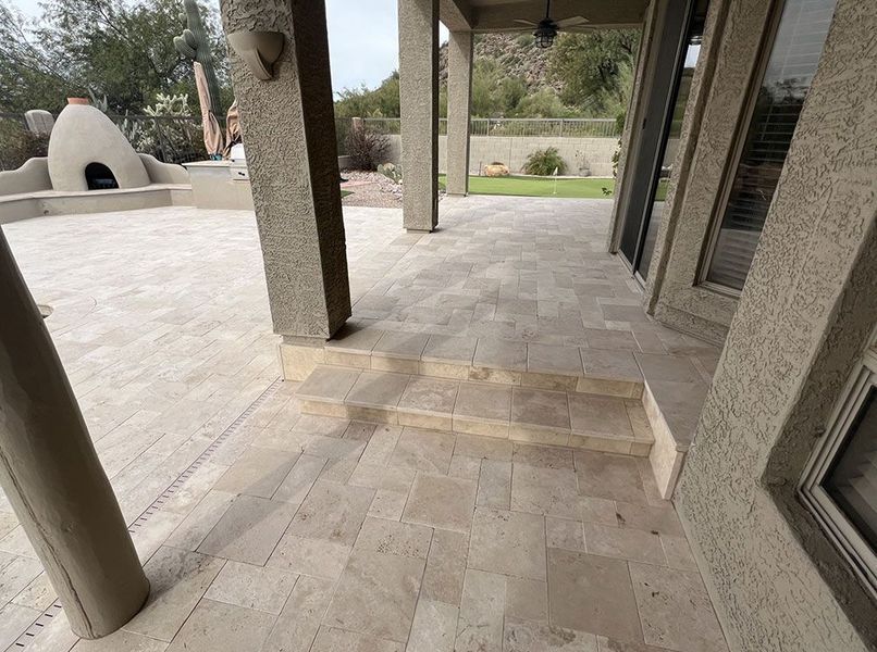 Patio with light-colored tile flooring, steps, columns, and a view of a yard and outdoor oven.