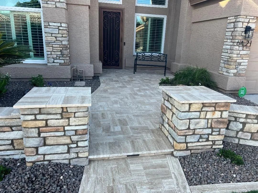 Stone walkway leading to a front door with stone pillars on either side; neutral tones.