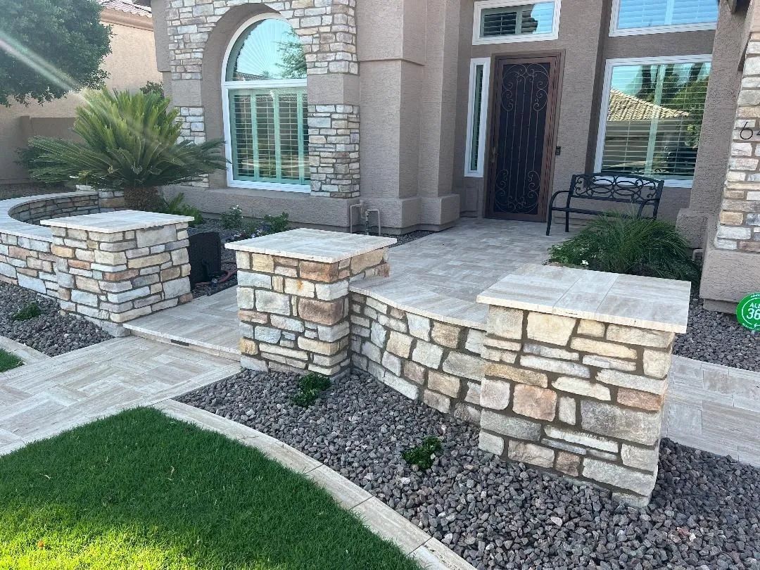 Stone columns and walkway leading to a house with a rounded window and dark front door.