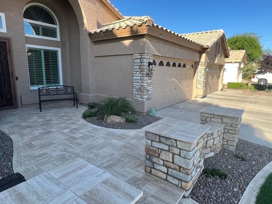 A beige stucco house with a tiled walkway and stone pillars. A black bench sits near the entrance.