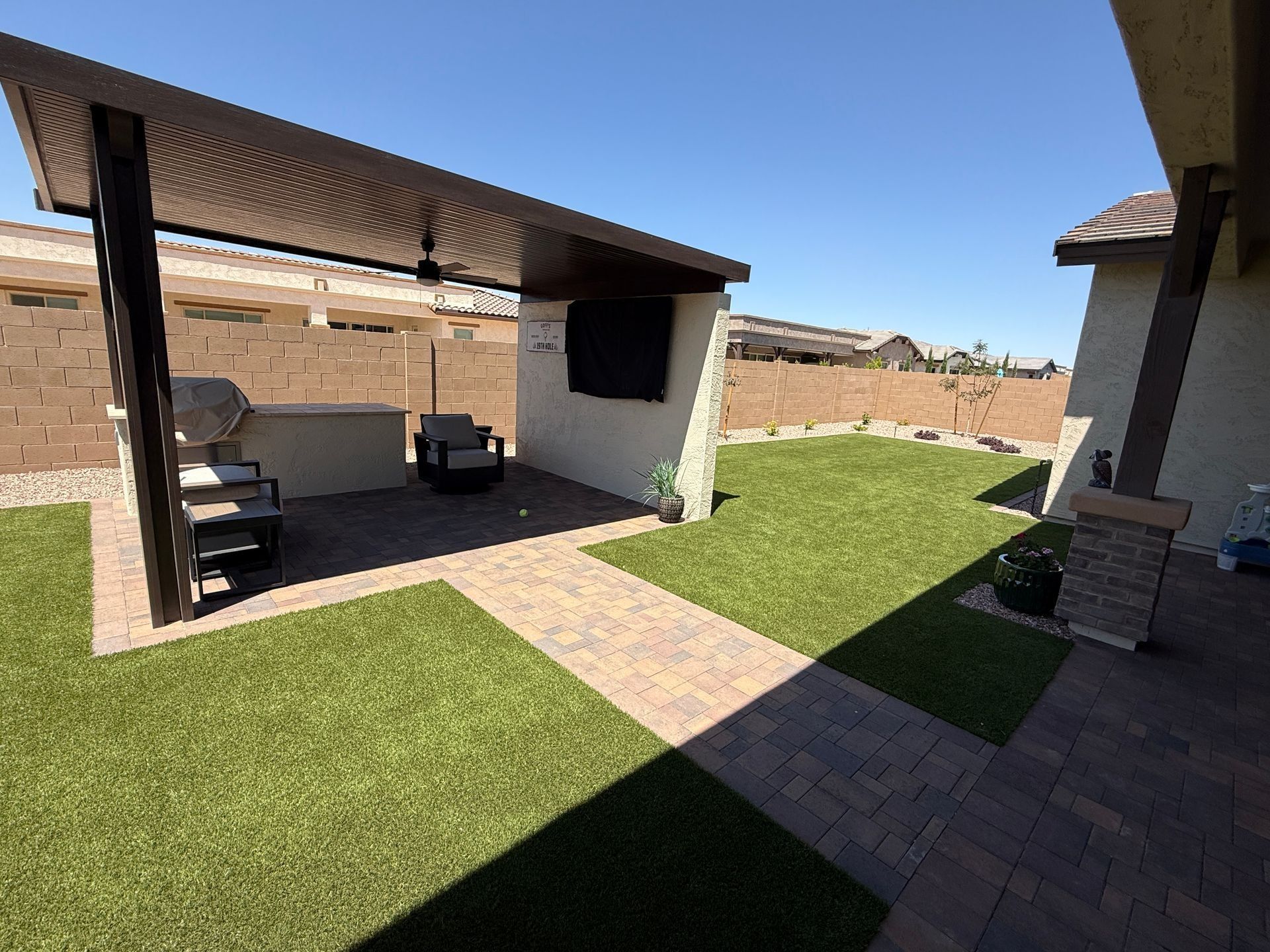 Backyard with a grilling area, paved path, and green turf lawn.