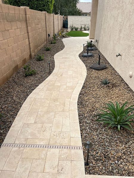 Stone pathway with landscaping between a tan wall and gravel bed.