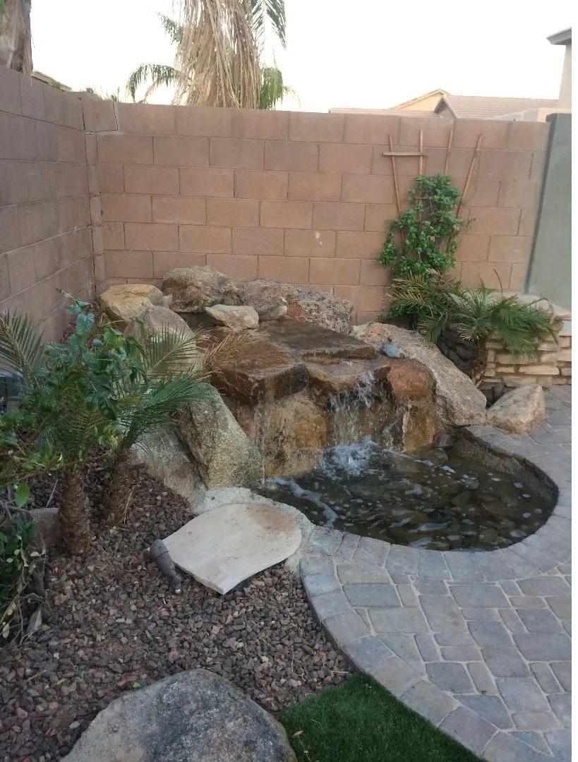 Water feature with waterfall and rocks in a backyard with a brick wall and paving stones.