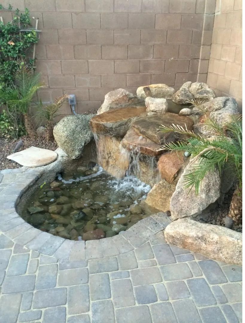 Small backyard water feature with waterfall cascading into a pond. Stone bricks surround.