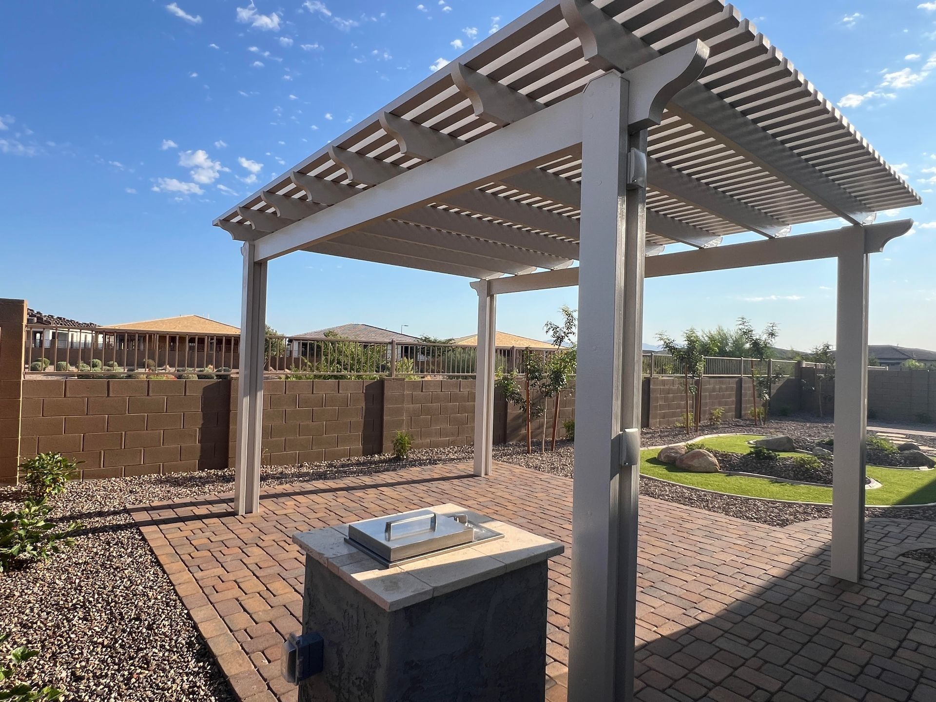 Pergola over a brick patio with a grill, in a backyard.