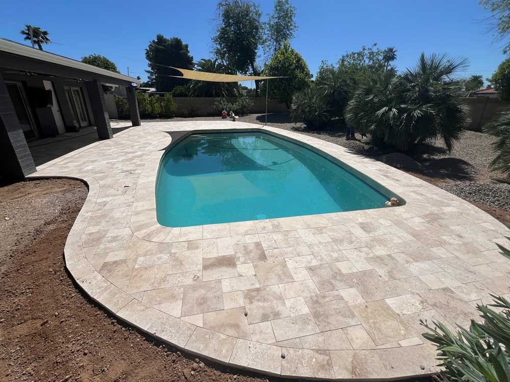 Pool with stone patio in a backyard setting on a sunny day.