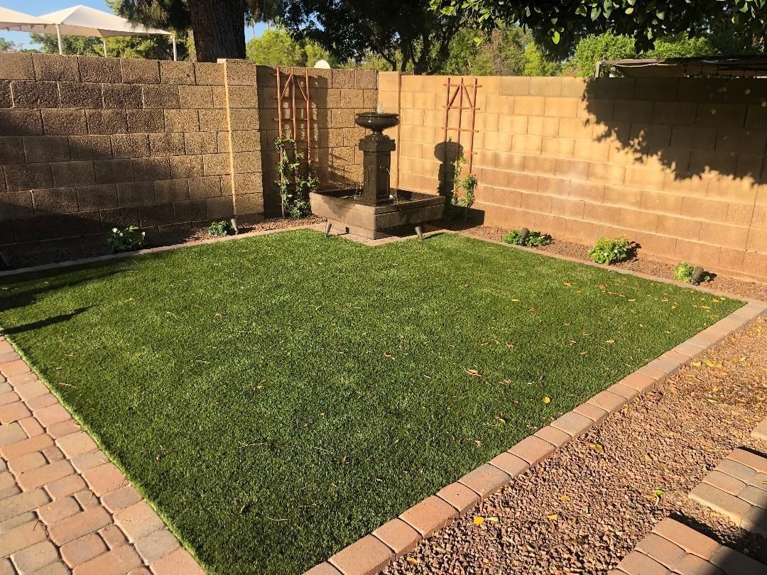 Lush green lawn in a walled backyard. A stone fountain is in the corner. Brick edging surrounds the grass.