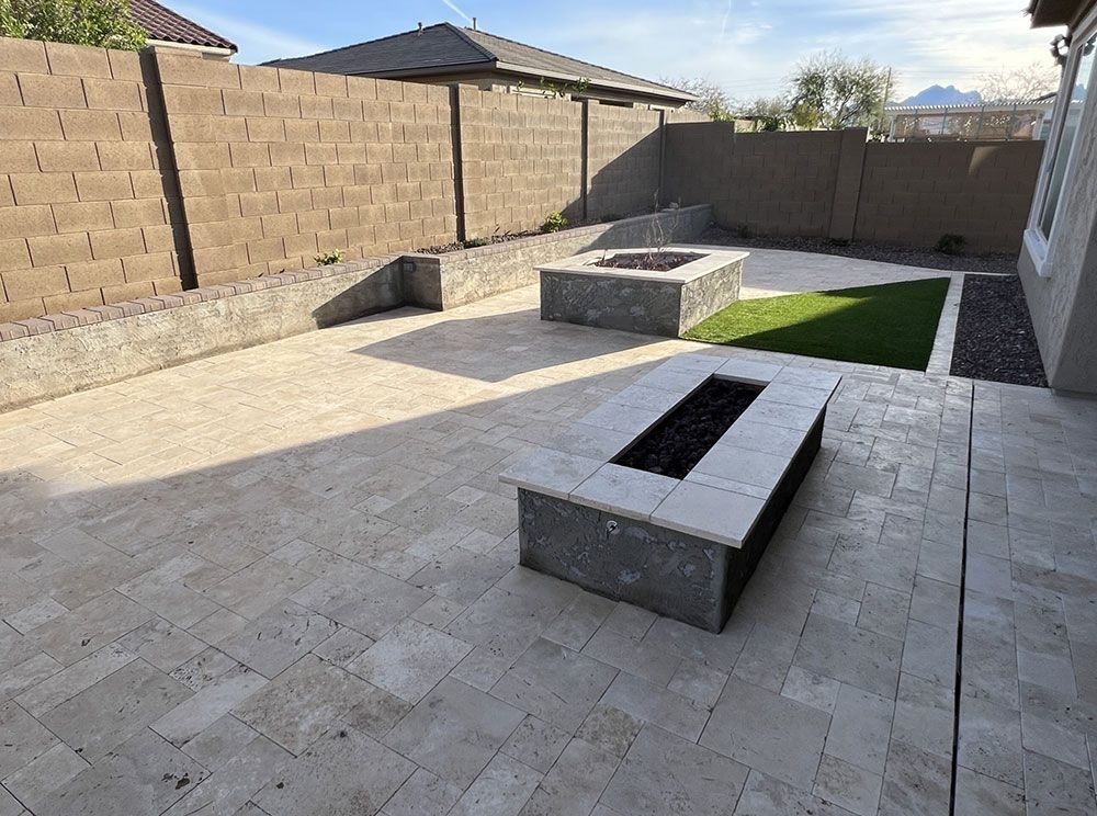 Backyard patio with travertine pavers, two fire pits, artificial turf, and a concrete block wall.