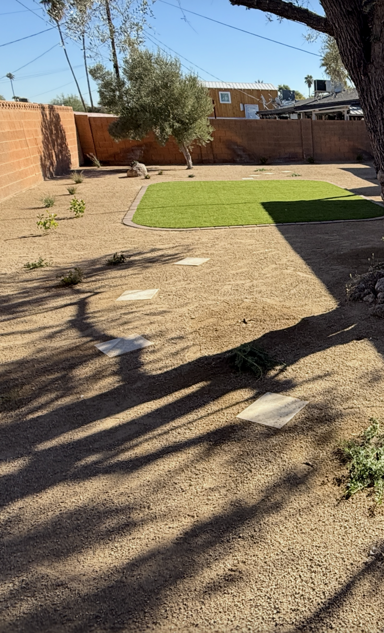 Backyard with gravel ground, a patch of green grass, and a brick wall under a blue sky.