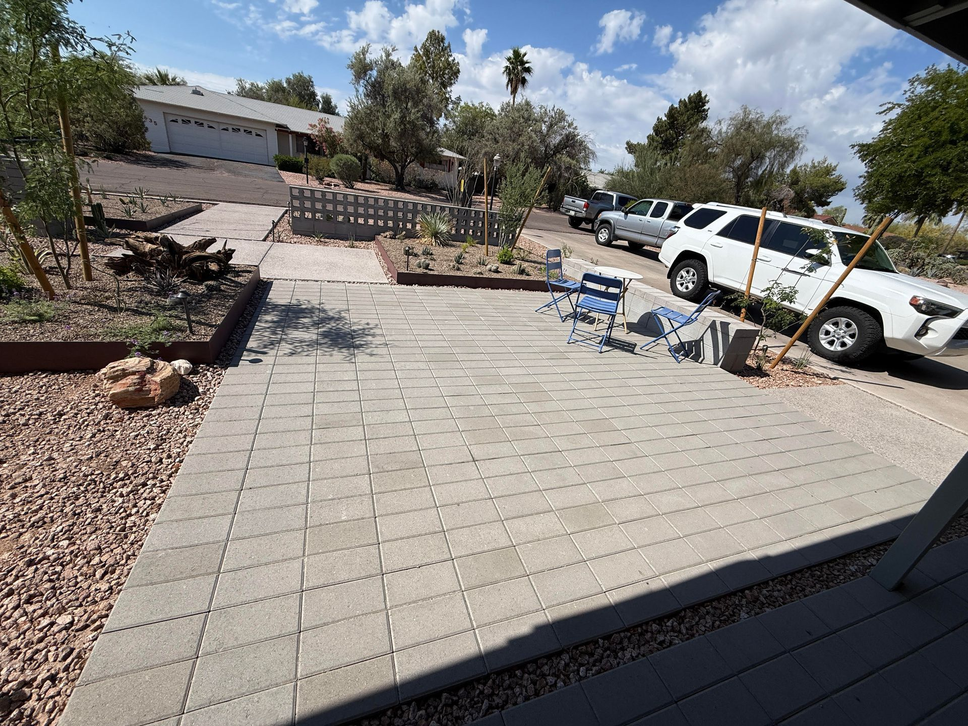 Brick patio and rock landscaping in front of a house. White SUV parked on the street.