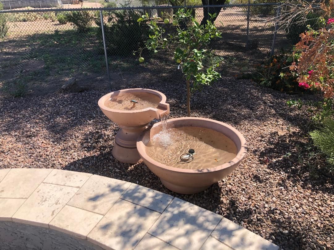 Two-tiered terra cotta water fountain in a backyard setting with a sunny appearance.