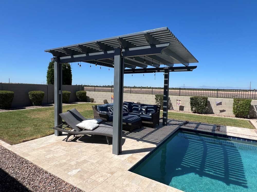 Pergola over a pool with seating and lounge chair, gray frame, blue cushions, sunny outdoor setting.