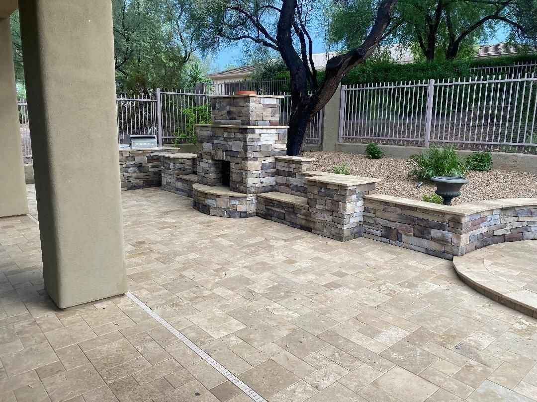 Patio with stone fireplace and seating, bordered by a decorative wooden fence.