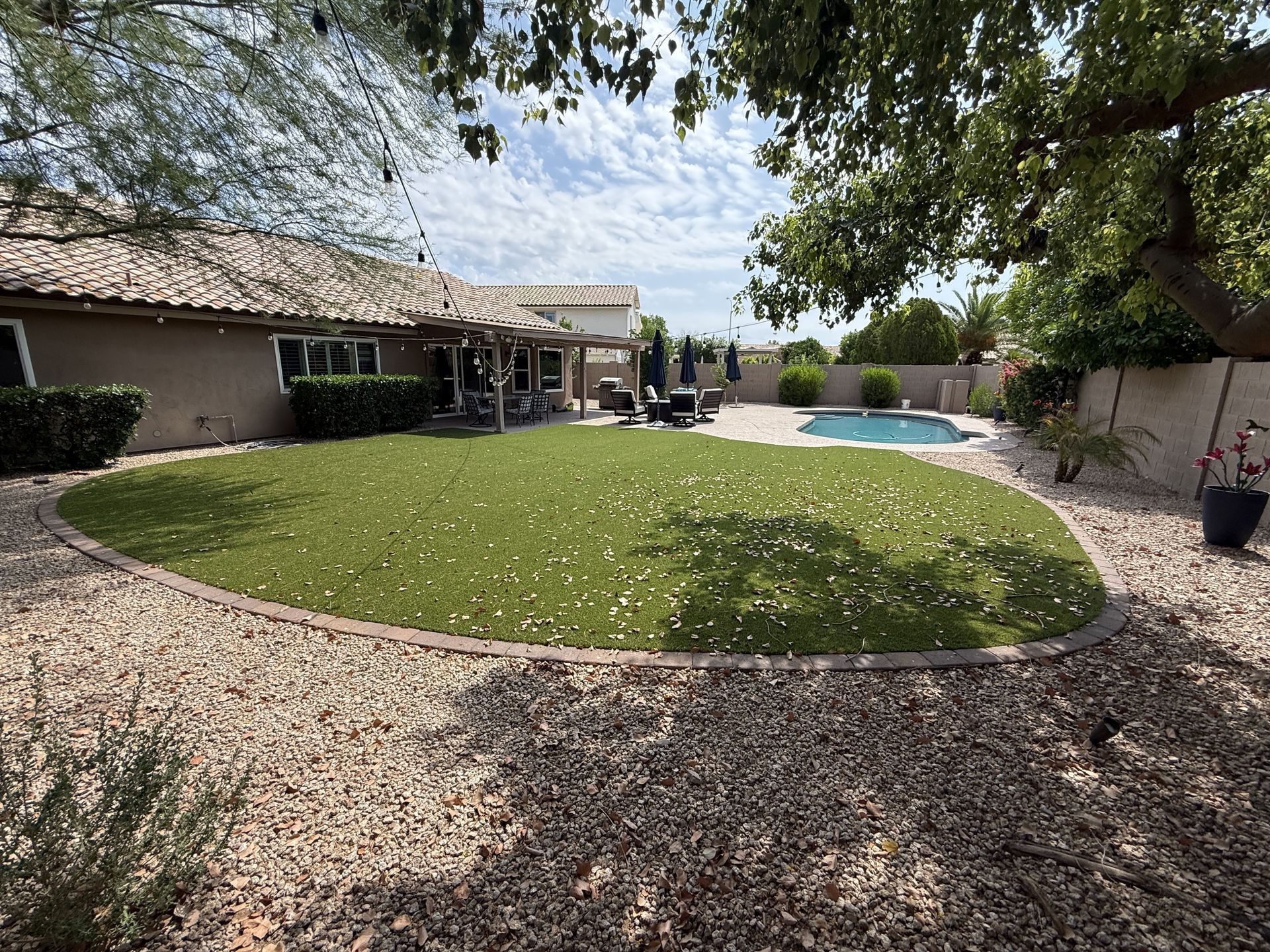 Backyard with green lawn, swimming pool, beige house, and gravel landscaping under a cloudy sky.