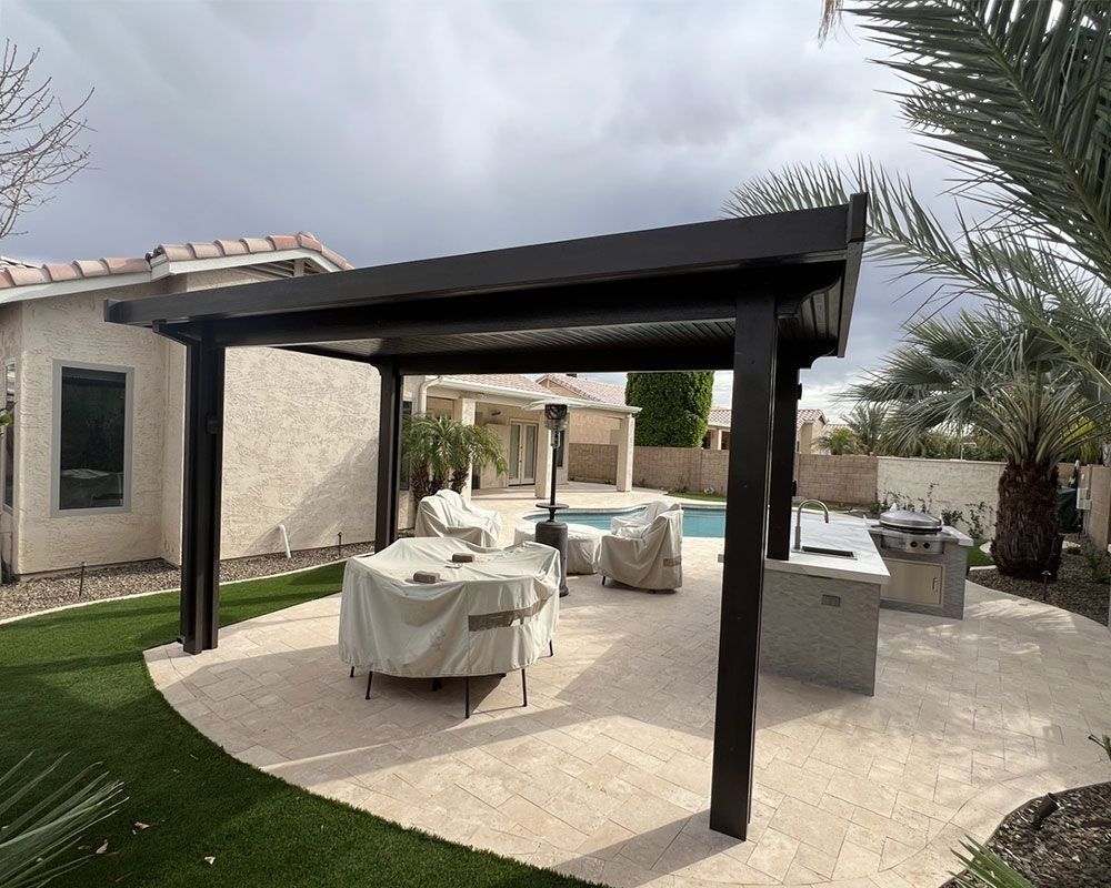 Black pergola over patio with seating, outdoor kitchen, and pool in the background.