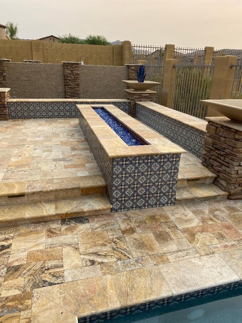 Patio with fire pit and steps, bordered by stone and decorative tile. Pool visible at bottom.