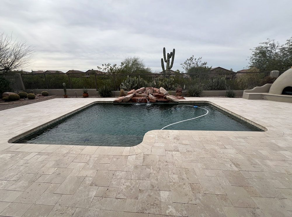 Rectangular pool with rock waterfall and surrounding patio in desert landscape.