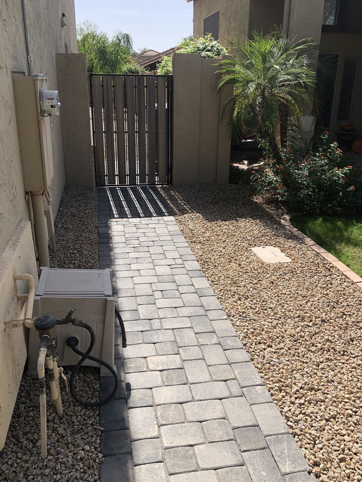 Brick walkway leading to a wooden gate, flanked by gravel and a utility box.