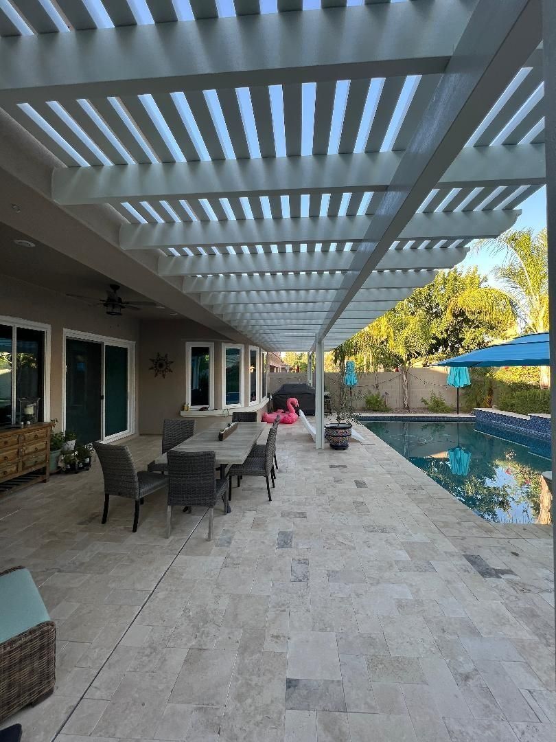 Patio with pergola, dining table, pool, and house. White and tan tones. Sunny outdoor scene.