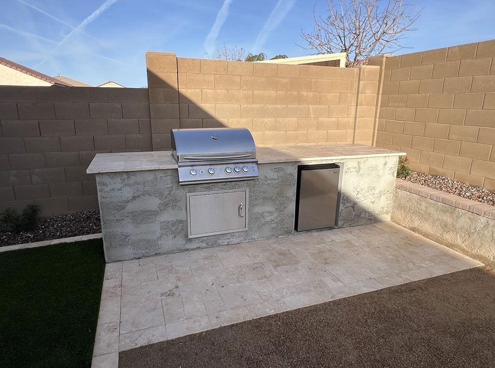Outdoor kitchen with built-in grill, refrigerator, and storage cabinet, set against a concrete wall.