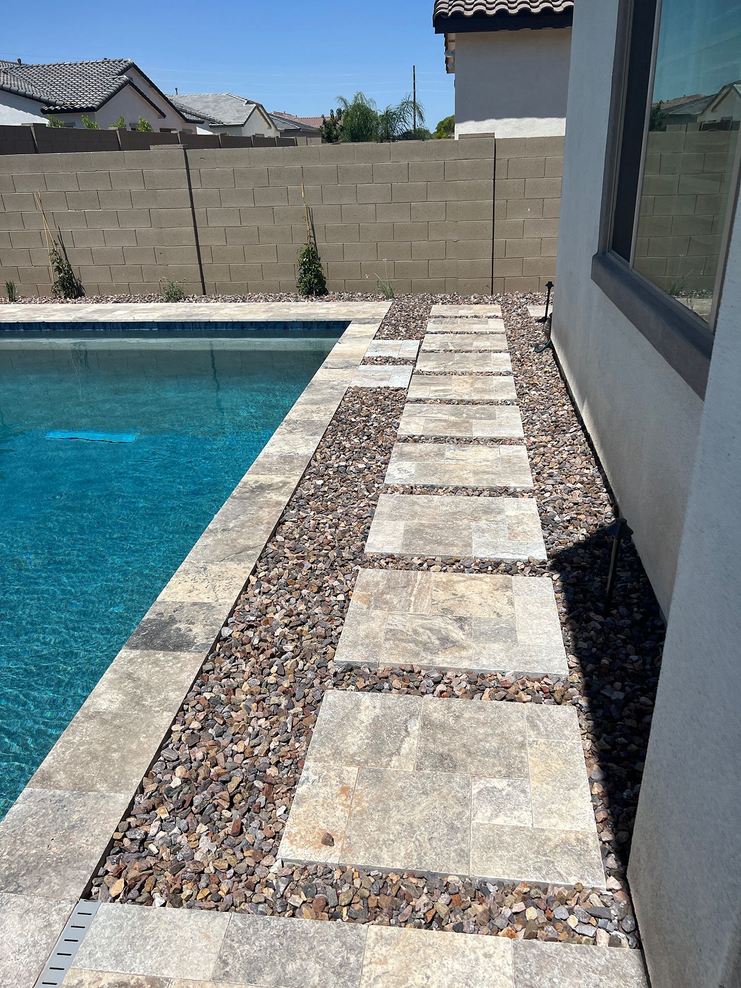 Poolside walkway with stone pavers, pebbles, and a pool on a sunny day.