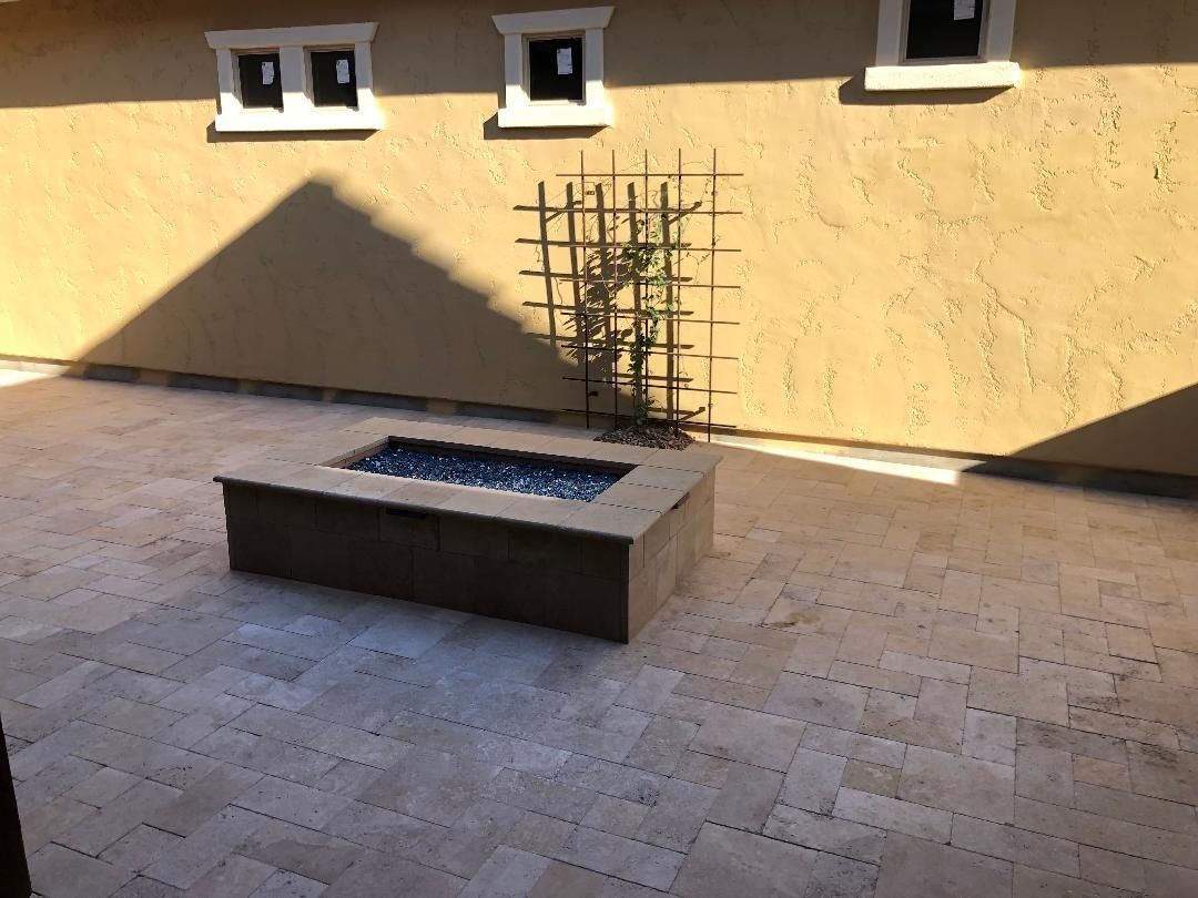 Stone patio with a rectangular fire pit, a trellis, and tan stucco wall with windows.