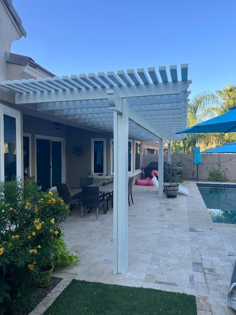 White pergola over a patio with a dining table, near a pool, under a blue sky.