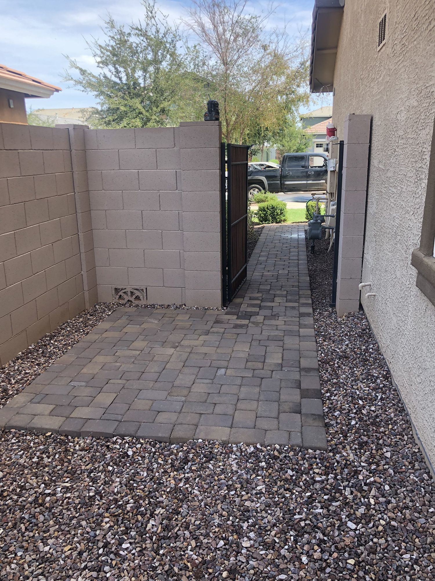 Stone patio with a block wall, open gate, and pathway with gravel.