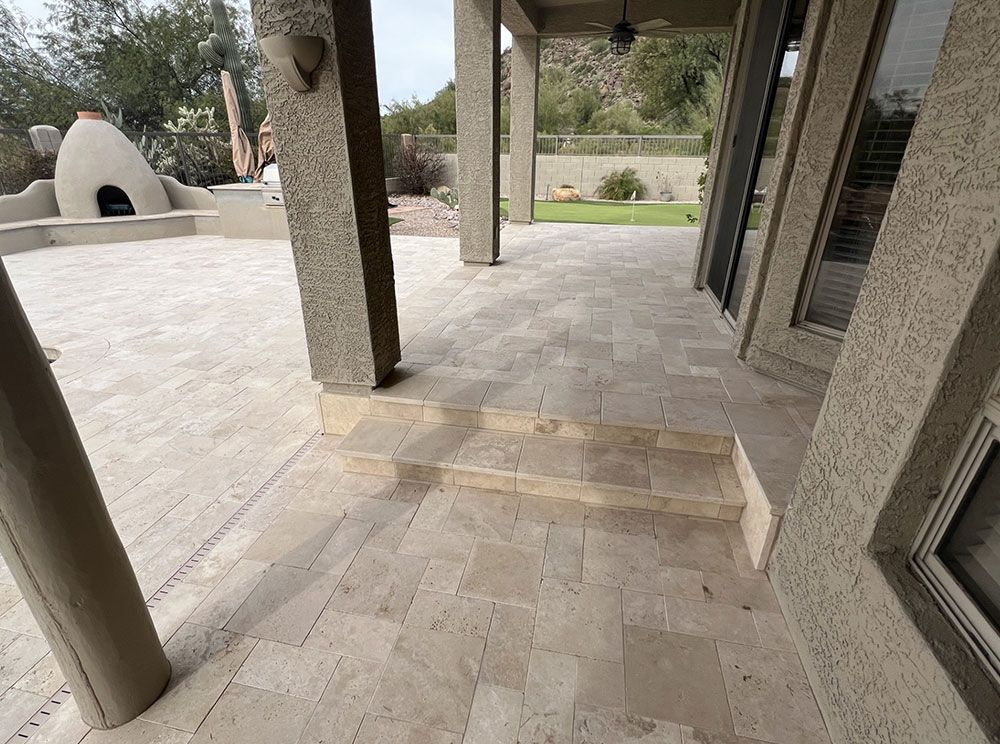 Covered patio with steps and stone flooring, leading to a yard with a built-in outdoor oven.