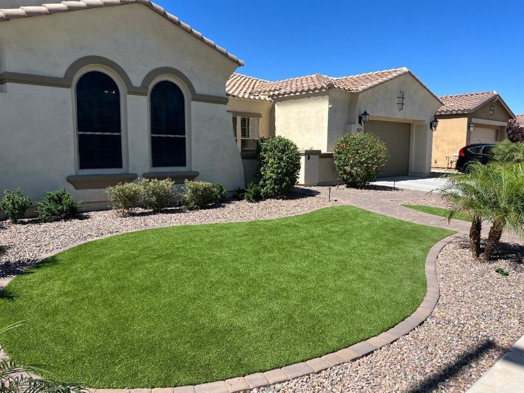 Beige house with arched windows and a lawn bordered by gravel and brick.