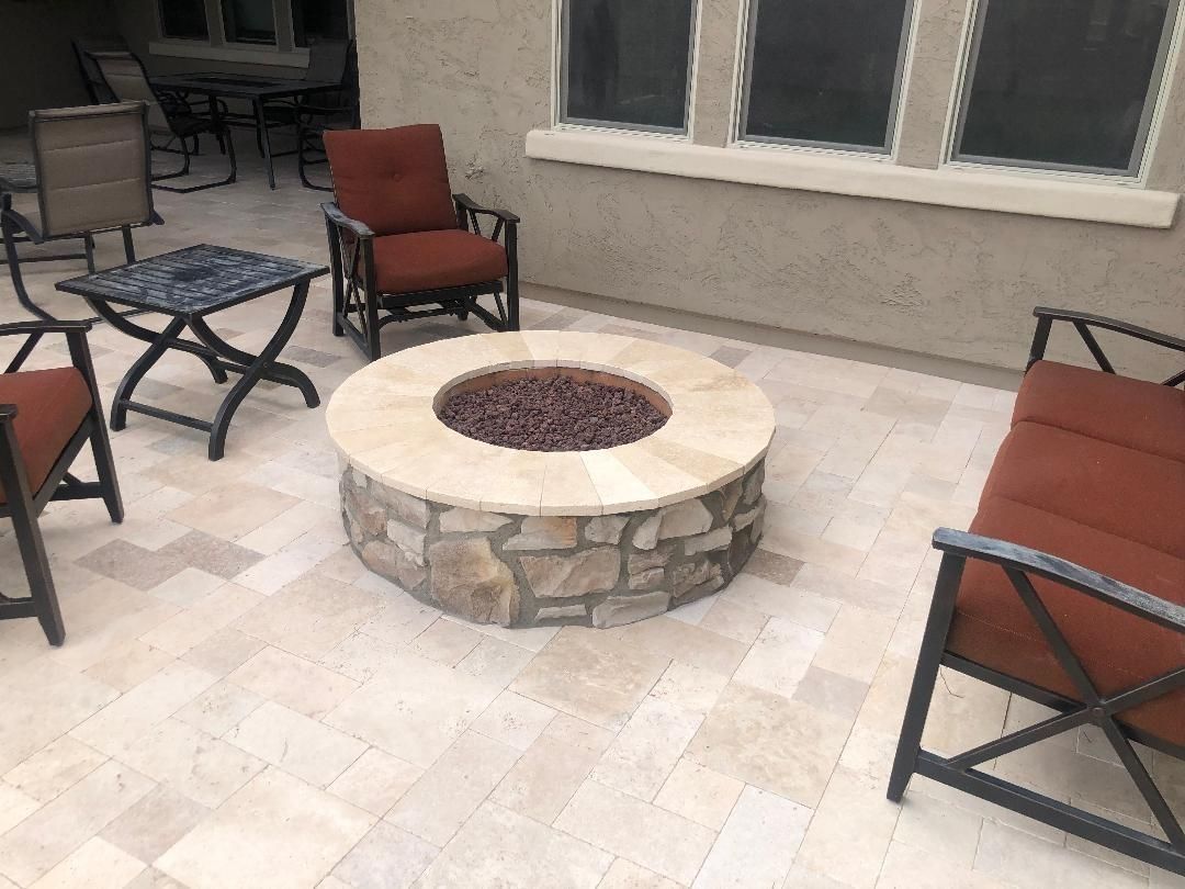 Stone fire pit on a patio, surrounded by chairs with rust-colored cushions.
