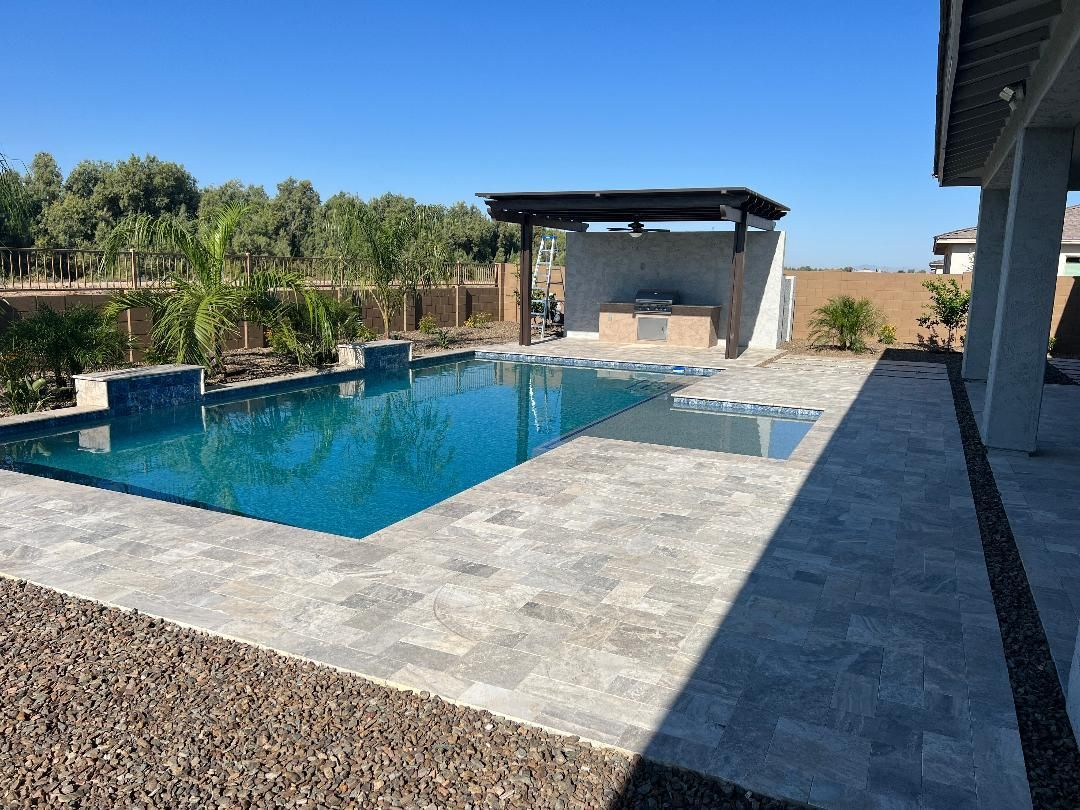 Swimming pool with patio, outdoor kitchen, and dark wood pergola under a bright blue sky.