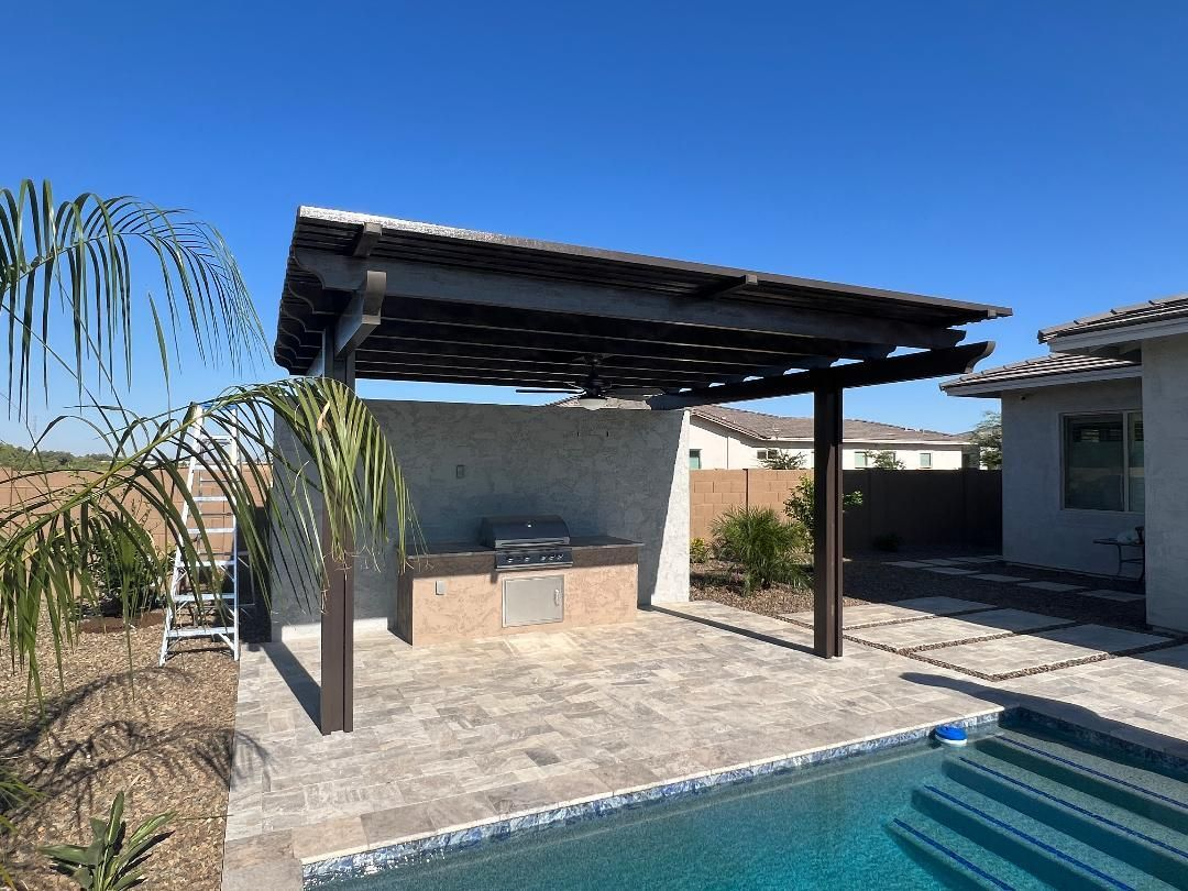 Outdoor kitchen with dark wood pergola, built-in grill, and swimming pool.