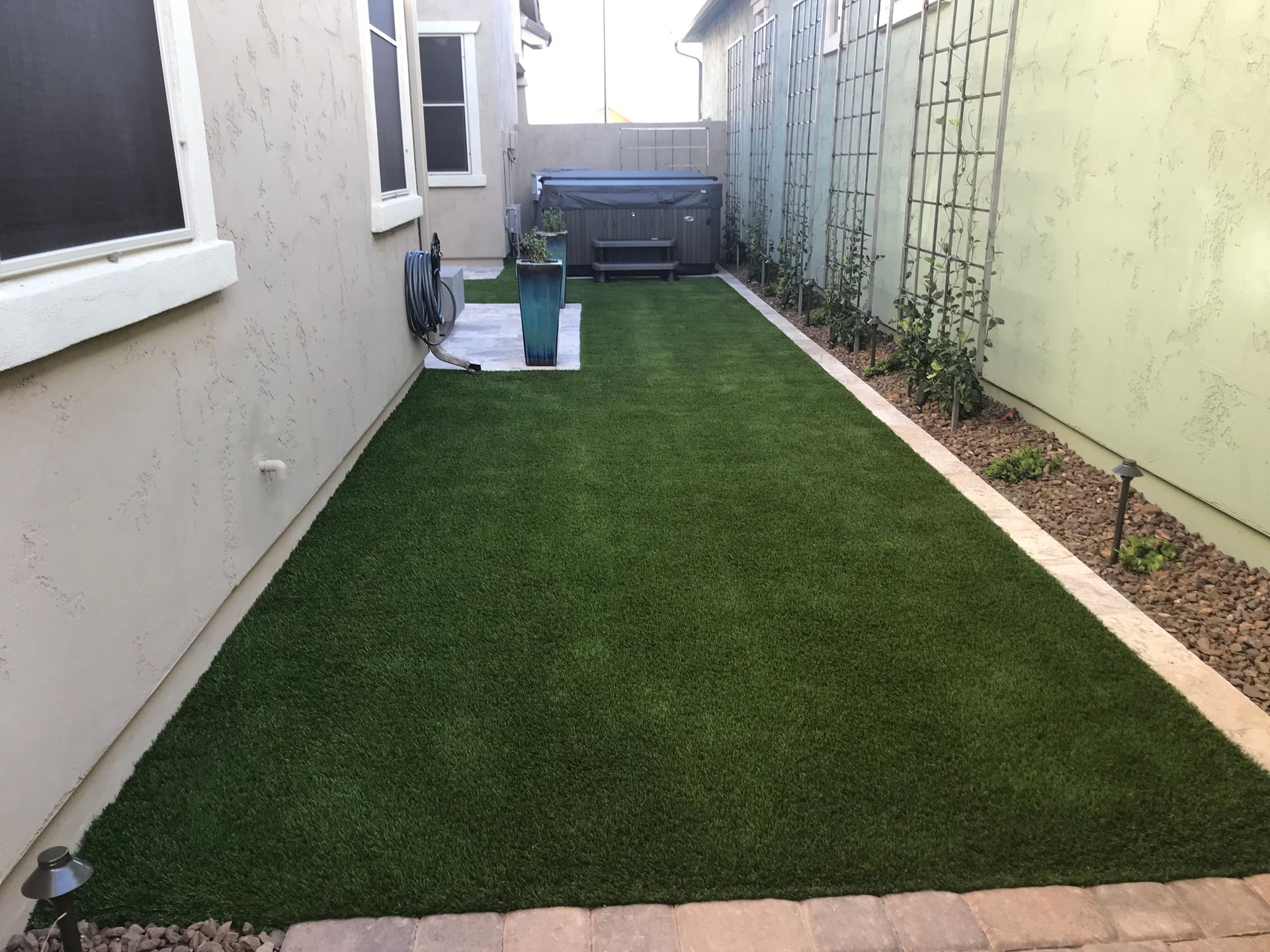 Backyard with green artificial turf, hot tub, and plants between two walls.