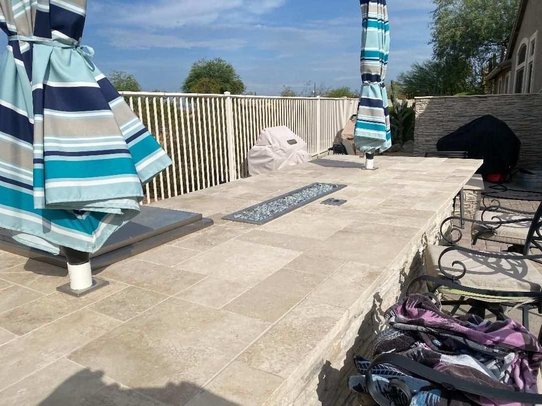 Patio with light beige stone, blue and white umbrellas, and a fire pit.
