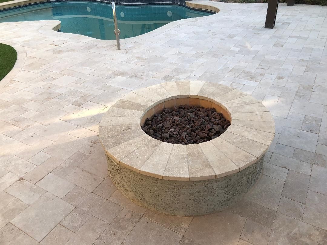 Stone fire pit on a stone patio beside a pool.