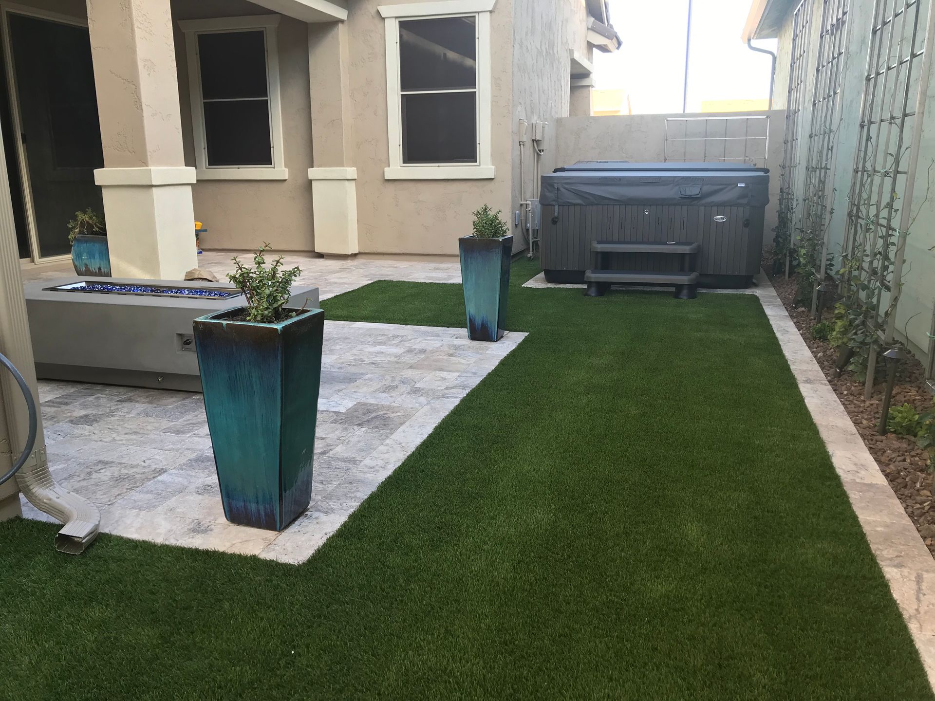 Backyard patio with hot tub, planters, fire pit, and artificial turf lawn.