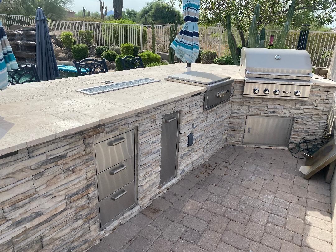 Outdoor kitchen with stone facade, stainless steel appliances, and brick patio.